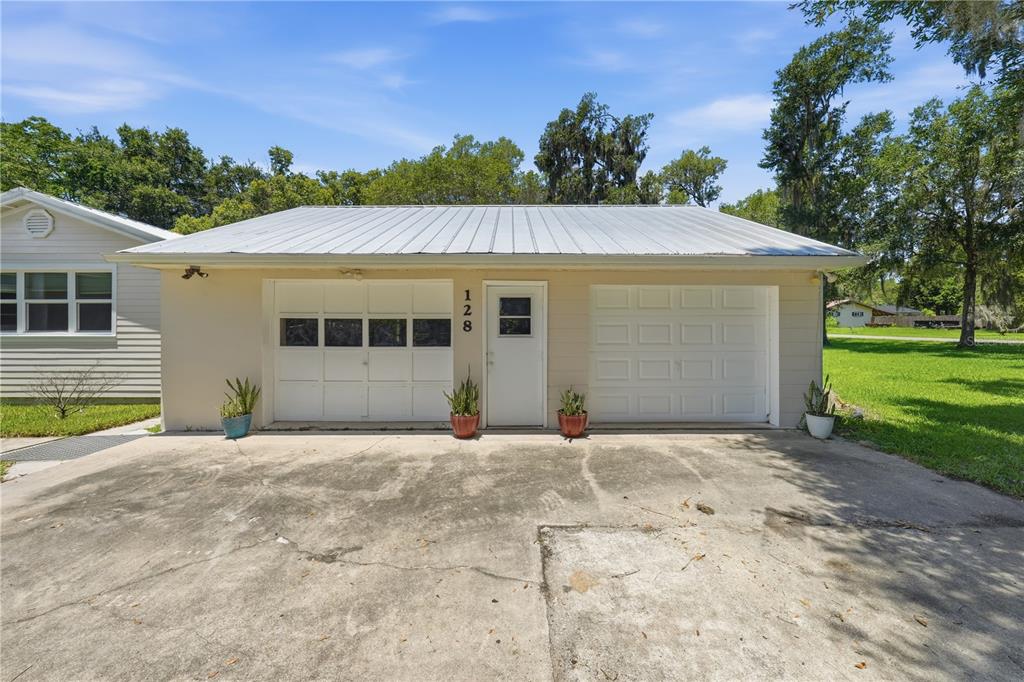 A detached two-car garage with a metal roof, beige siding, and a central entry door — 128 N LAKEVIEW DRIVE, LAKE HELEN, FL