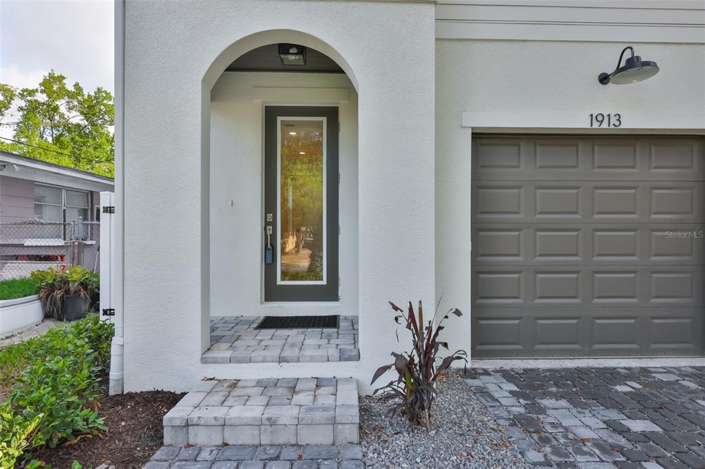 The exterior of a home features a gray garage door, a front door, and pavers — 1913 W BEACH STREET, TAMPA, FL