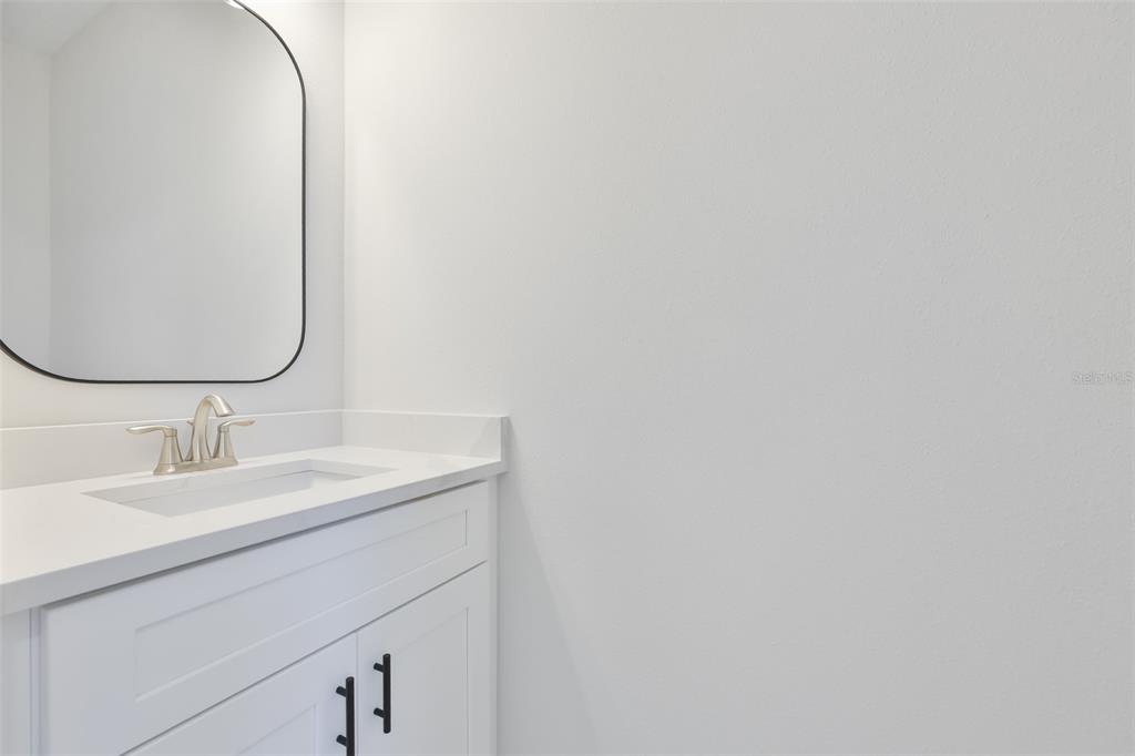 A modern bathroom vanity with a white countertop, black hardware, and a rounded mirror — 1913 W BEACH STREET, TAMPA, FL