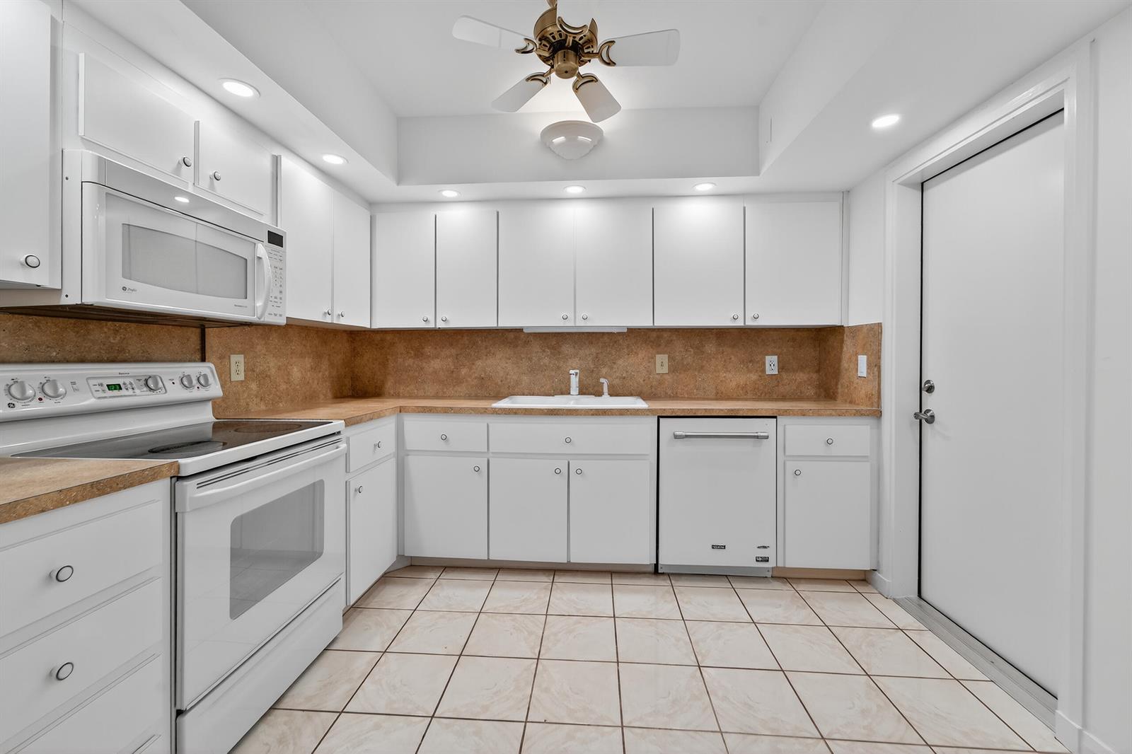 A kitchen features white cabinets, white appliances, tan countertops, and light-colored tile flooring — 6 Concourse Drive # A, Jupiter FL 33469, JUPITER, FL