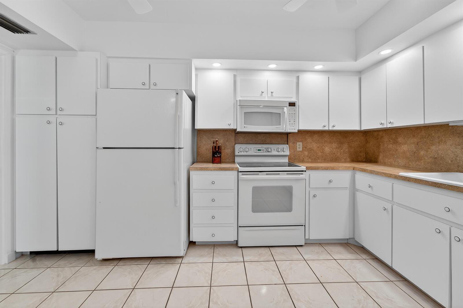 A kitchen with white cabinets, white appliances, and tan countertops over a tiled floor — 6 Concourse Drive # A, Jupiter FL 33469, JUPITER, FL