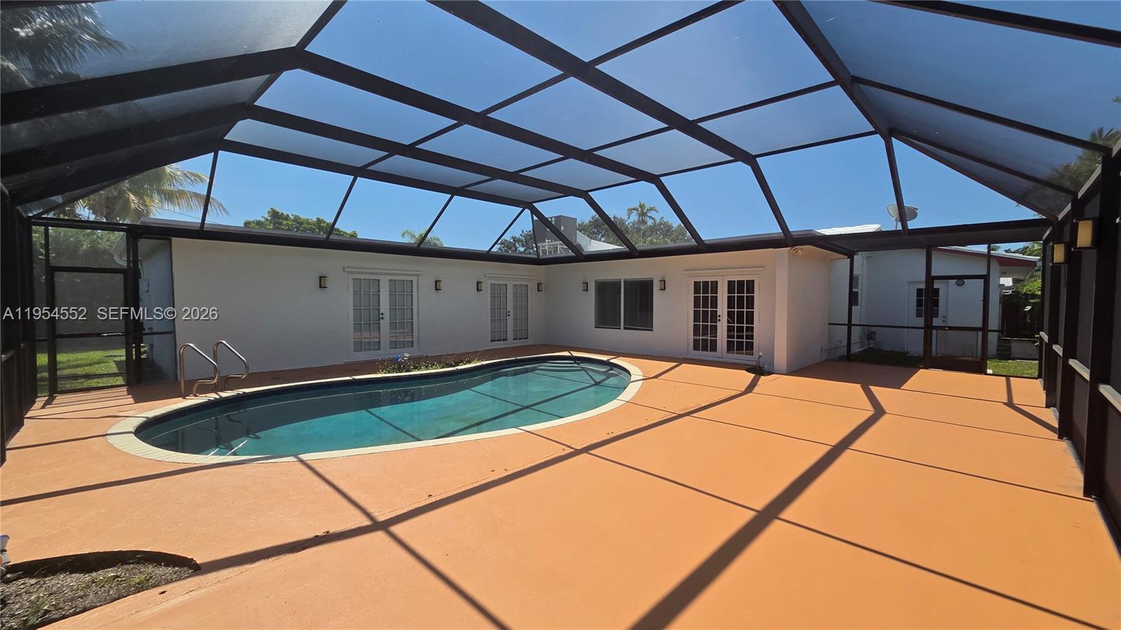 A screened-in patio features a kidney-shaped swimming pool and light-colored exterior walls — 1245 Coral Ln, Hollywood FL 33019, HOLLYWOOD, FL
