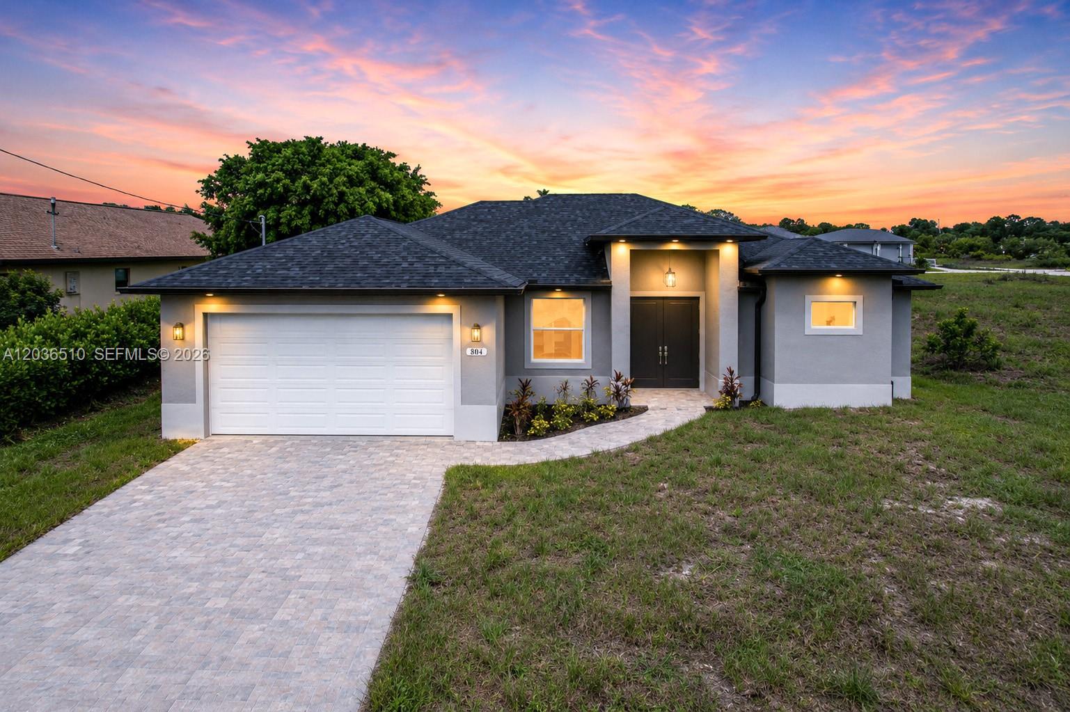 A modern single-story house with a gray exterior, dark roof, and a paved driveway — 804 Curtis Ave N, Lehigh Acres FL 33971, LEHIGH ACRES, FL