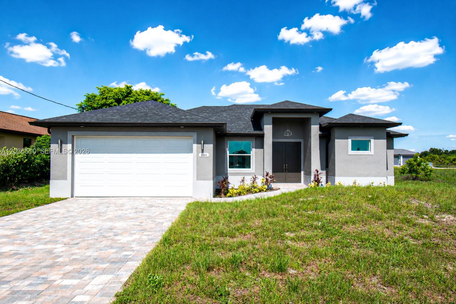 A single-story gray house features a white garage door, dark double entry doors, and landscaping — 804 Curtis Ave N, Lehigh Acres FL 33971, LEHIGH ACRES, FL