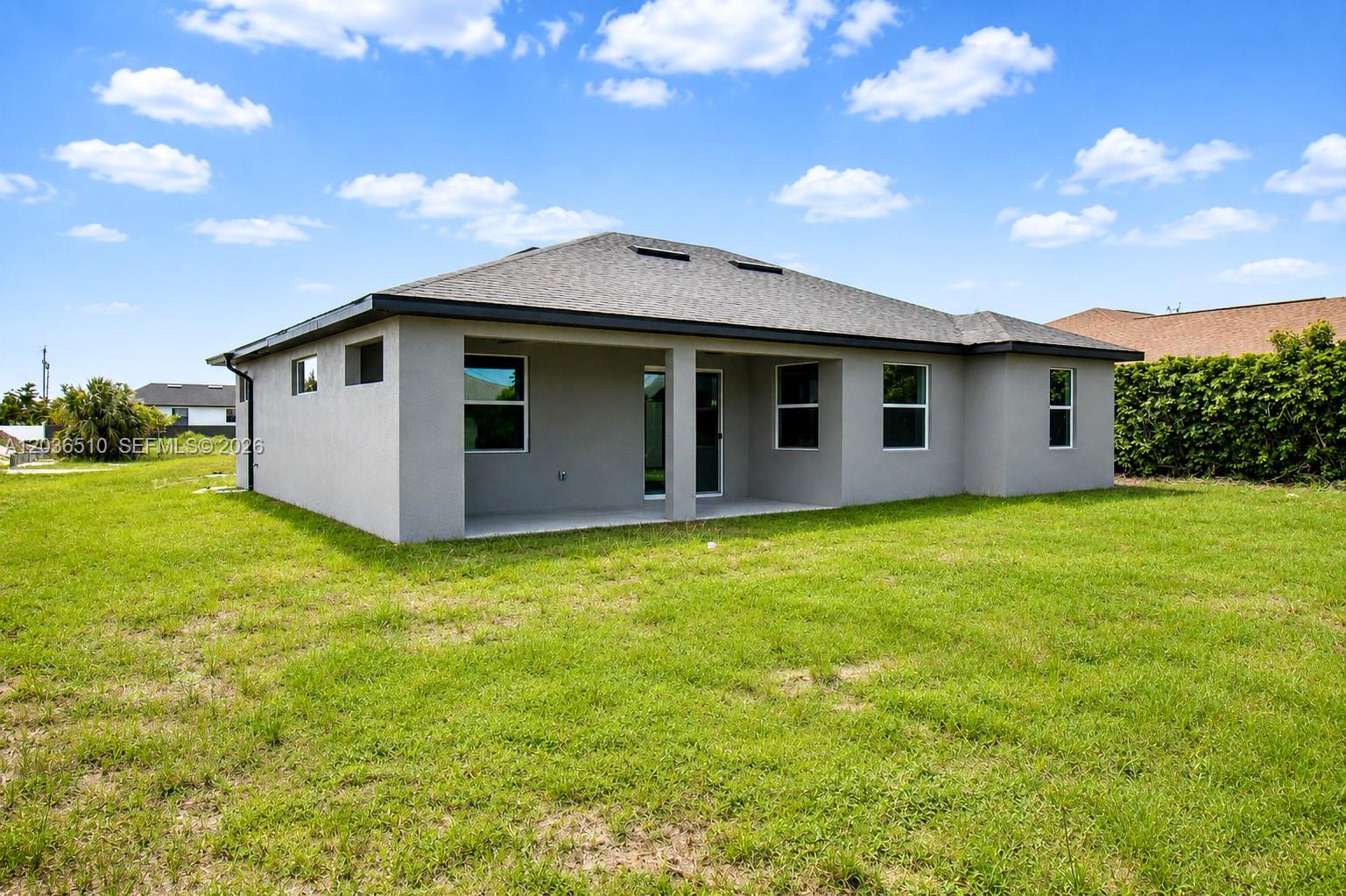 The exterior rear view of a single-story gray house features a covered patio and lawn — 804 Curtis Ave N, Lehigh Acres FL 33971, LEHIGH ACRES, FL