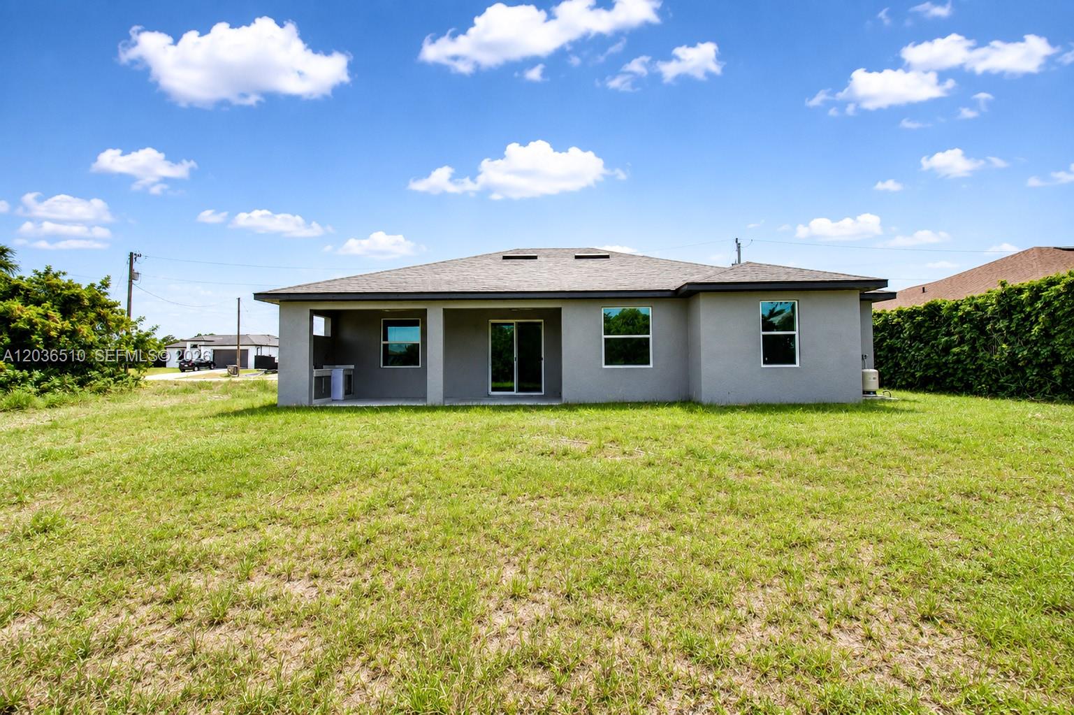 The rear exterior of a single-story gray house features a covered patio and lawn — 804 Curtis Ave N, Lehigh Acres FL 33971, LEHIGH ACRES, FL
