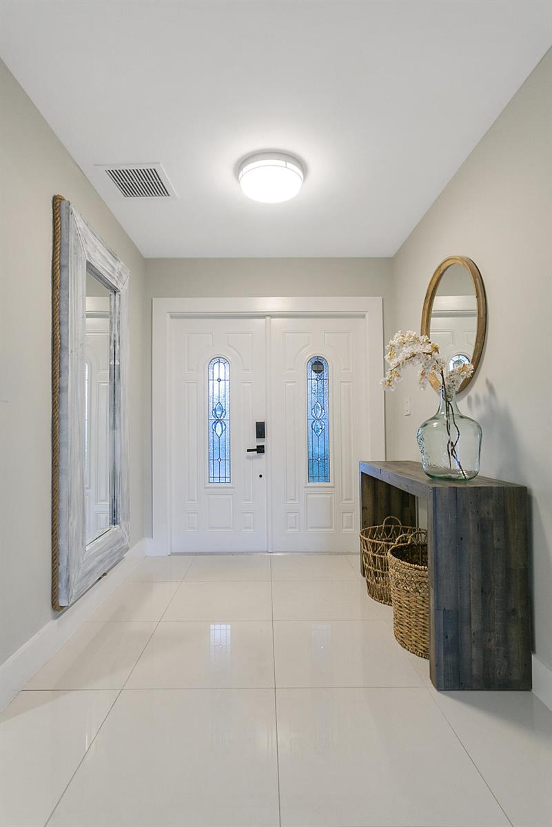 A bright entryway features white tile floors, a double front door, and a wooden console table — 231 SE 8th Street, Dania Beach FL 33004, DANIA BEACH, FL
