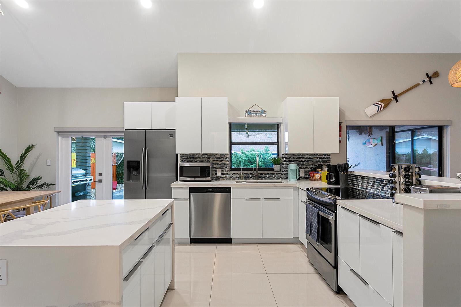A modern kitchen features white cabinets, stainless steel appliances, a quartz island, and tile flooring — 231 SE 8th Street, Dania Beach FL 33004, DANIA BEACH, FL