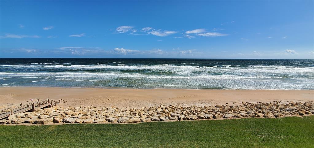 A grassy lawn overlooks a rocky seawall, sandy beach, and the ocean under a blue sky — 6727 TURTLEMOUND ROAD UNIT 416, NEW SMYRNA BEACH, FL