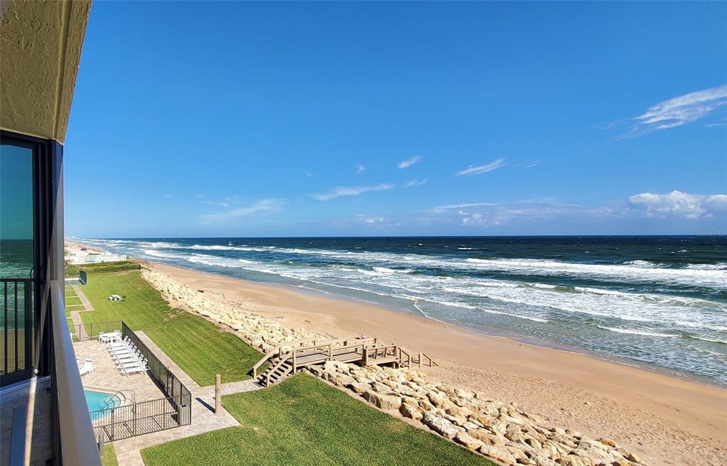 A high-angle view of a beach and ocean from a balcony with a pool below — 6727 TURTLEMOUND ROAD UNIT 416, NEW SMYRNA BEACH, FL