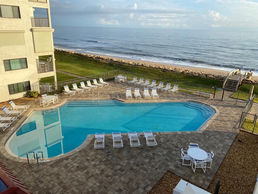 An elevated view of a swimming pool and patio area adjacent to a beachside building — 6727 TURTLEMOUND ROAD UNIT 416, NEW SMYRNA BEACH, FL