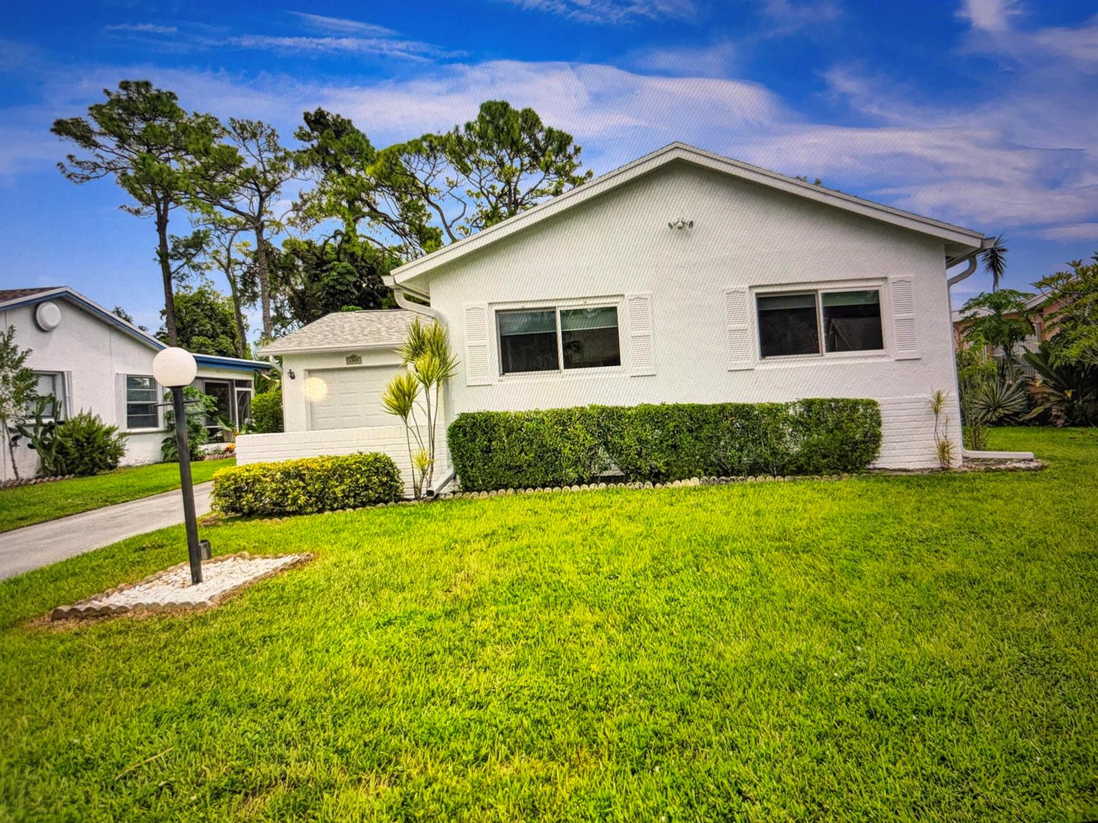 A white, single-story house with a green lawn, a hedge, and a paved driveway — 6309 Silver Moon Lane, FL 33463, FL