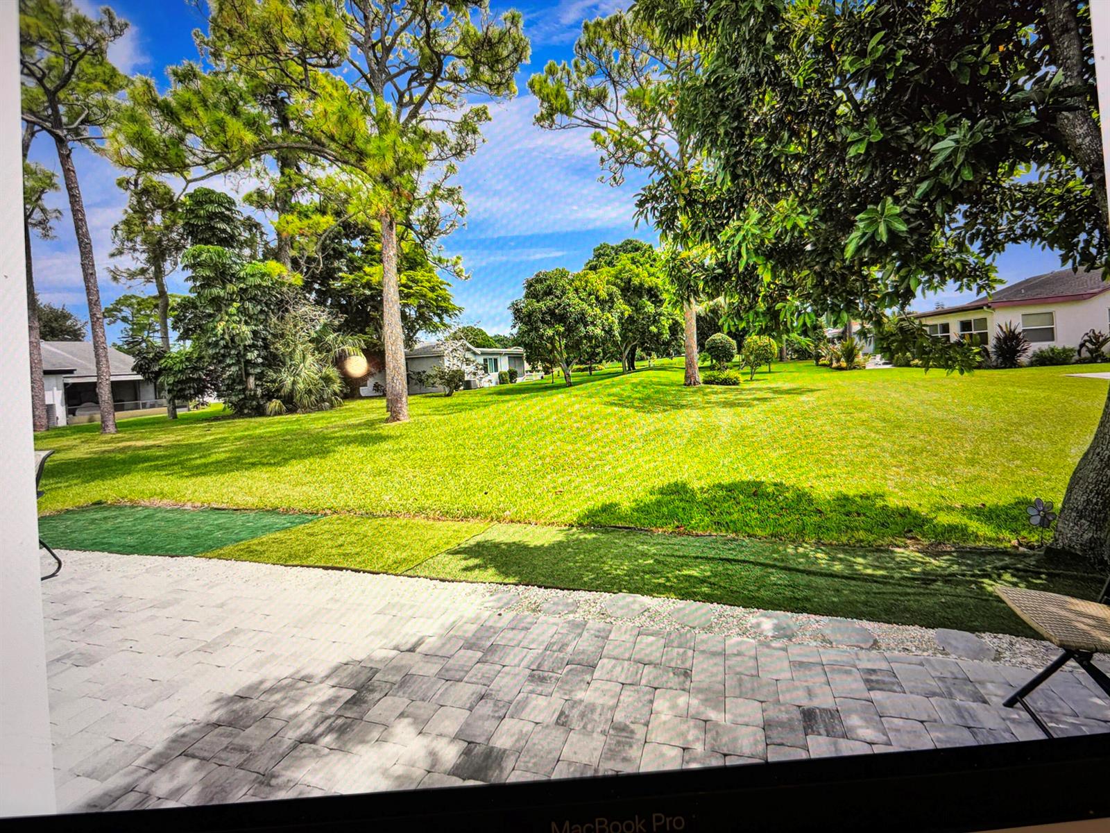 A paved patio overlooks a large, grassy backyard with mature trees and neighboring houses — 6309 Silver Moon Lane, FL 33463, FL
