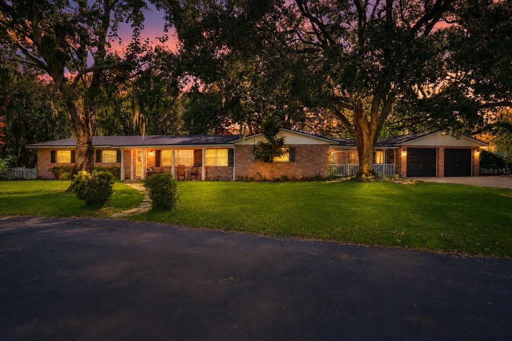 A single-story brick house with a two-car garage sits behind a lawn with large trees — 5315 POST LANE, LAKELAND, FL