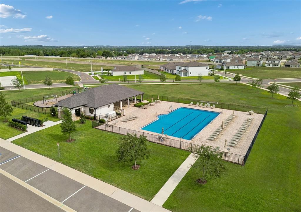 An aerial view of a community pool, clubhouse, playground, and parking lot in a neighborhood — 12338 STIRRUP DRIVE, DADE CITY, FL