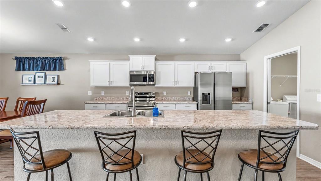 A kitchen features white cabinets, stainless steel appliances, a large island, and four bar stools — 3863 WILLOW RIDGE DRIVE, LAKELAND, FL