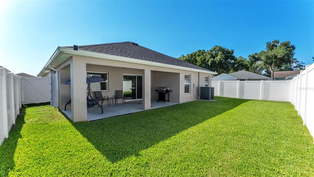 A backyard view of a house with a covered patio, lawn, and white vinyl fencing — 3863 WILLOW RIDGE DRIVE, LAKELAND, FL