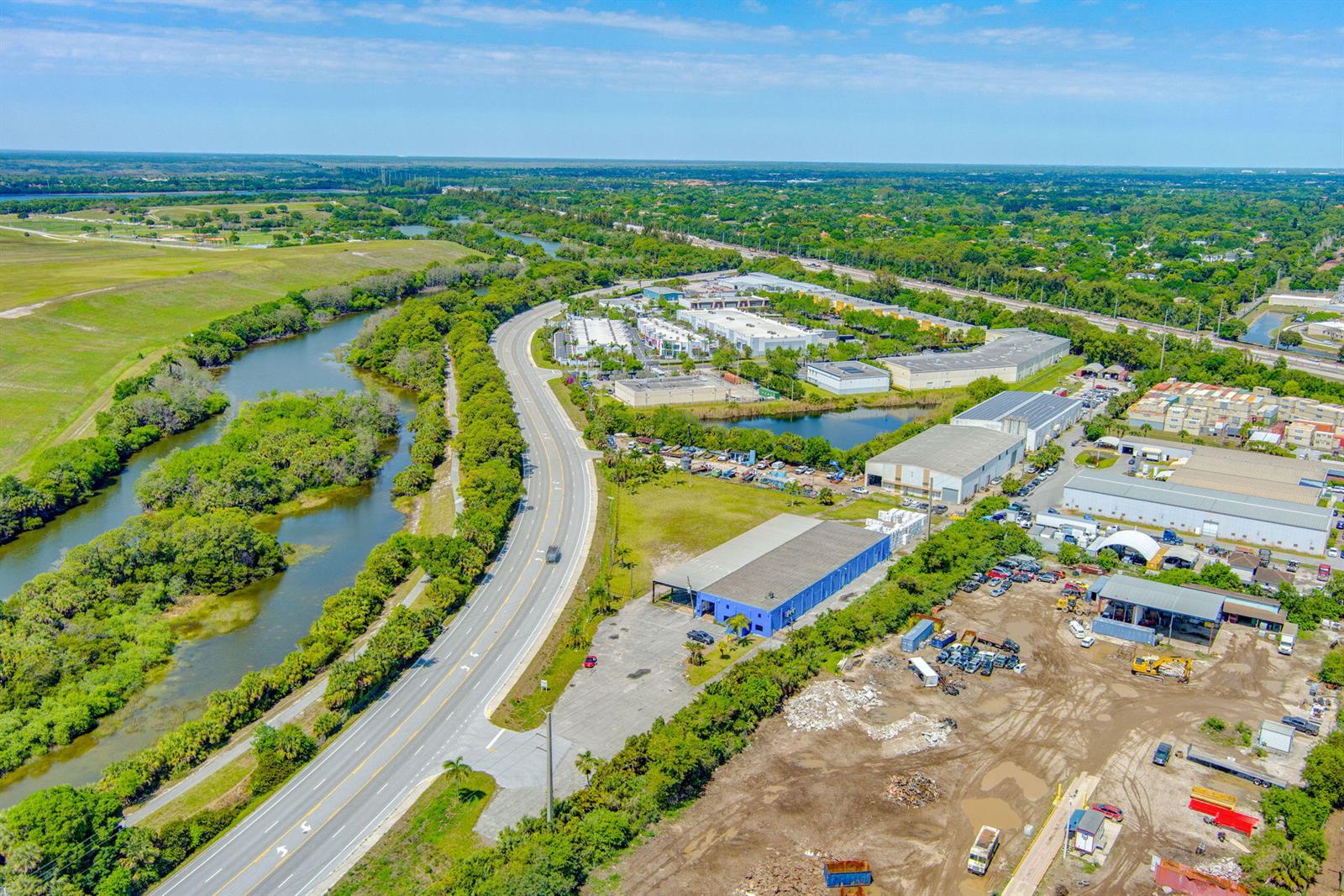 An aerial view shows a road winding past a river, industrial buildings, and a dirt lot — 7030 Haverhill Road, Riviera Beach FL 33407, RIVIERA BEACH, FL