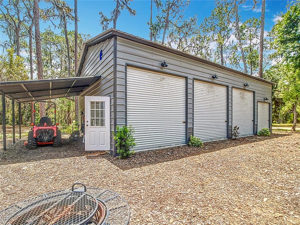 A metal garage with three roll-up doors, a side entry door, and an attached carport — 7374 CIRCLE DRIVE, LADY LAKE, FL