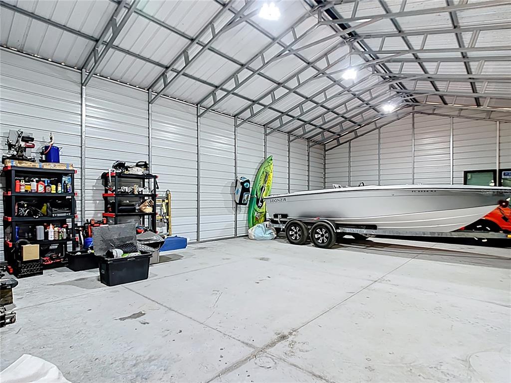 A large metal garage contains a boat on a trailer, a kayak, and storage shelving — 7374 CIRCLE DRIVE, LADY LAKE, FL