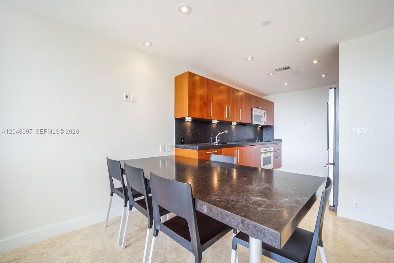 A kitchen features wood cabinets, dark countertops, and a dining table with black chairs — 151 Crandon Blvd # 439, Key Biscayne FL 33149, KEY BISCAYNE, FL