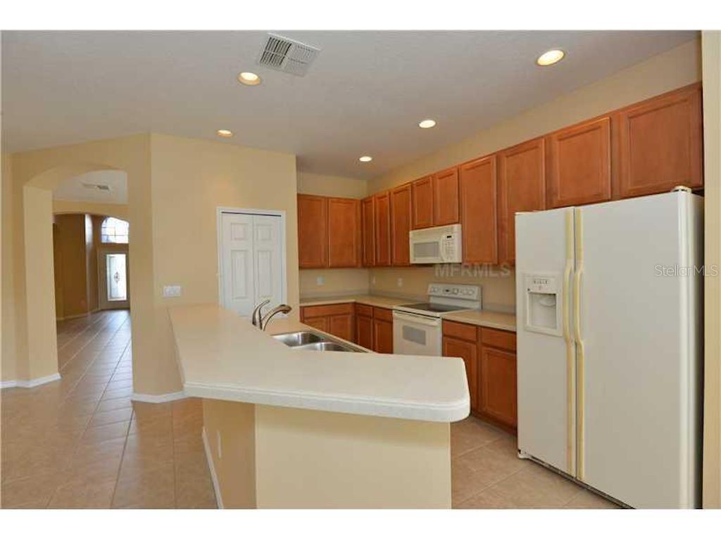 A kitchen with wood cabinets, white appliances, and a breakfast bar overlooking a tiled floor — 3132 SAGO POINT COURT, LAND O LAKES, FL