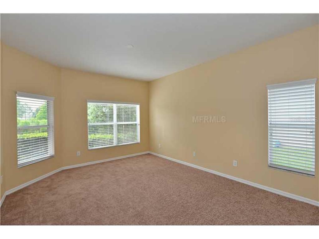 An empty bedroom with beige walls, tan carpeting, and three windows with white blinds — 3132 SAGO POINT COURT, LAND O LAKES, FL