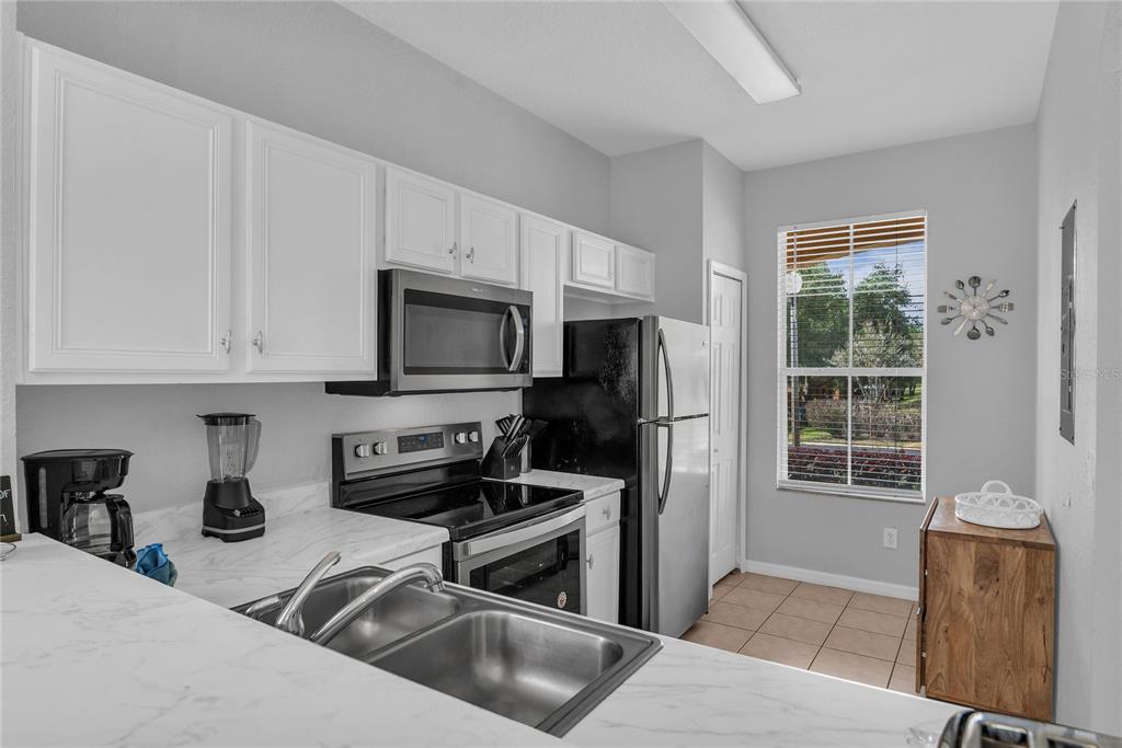 A kitchen features white cabinets, marble-look countertops, stainless steel appliances, and a window with blinds — 457 LA MIRAGE STREET, DAVENPORT, FL