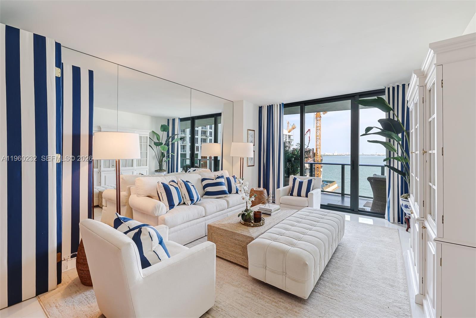 A living room features white furniture, blue-striped curtains, a mirrored wall, and a balcony view — 460 NE 28 # 704, Miami FL 33137, MIAMI, FL