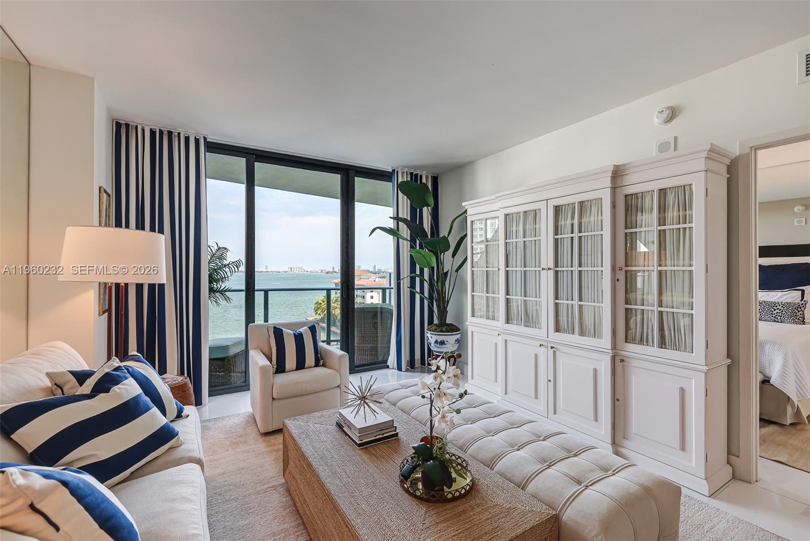 A living room features a white cabinet, tufted ottoman, and floor-to-ceiling windows overlooking the ocean — 460 NE 28 # 704, Miami FL 33137, MIAMI, FL