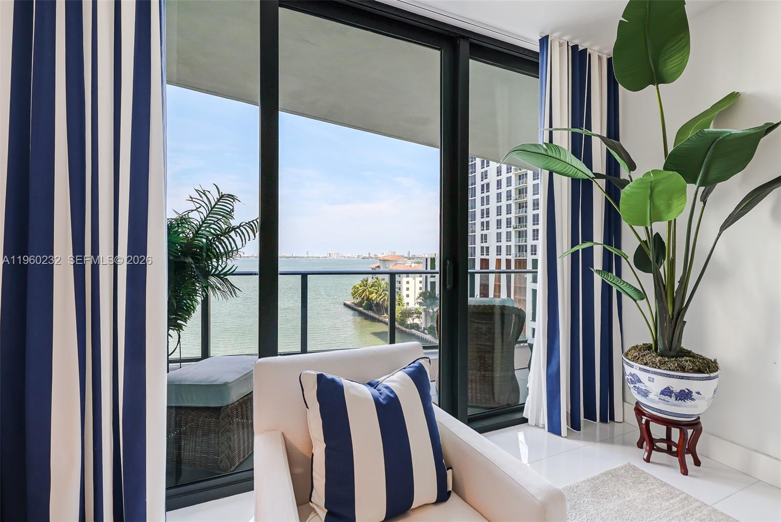 A white armchair with a striped pillow sits before a balcony overlooking the water — 460 NE 28 # 704, Miami FL 33137, MIAMI, FL