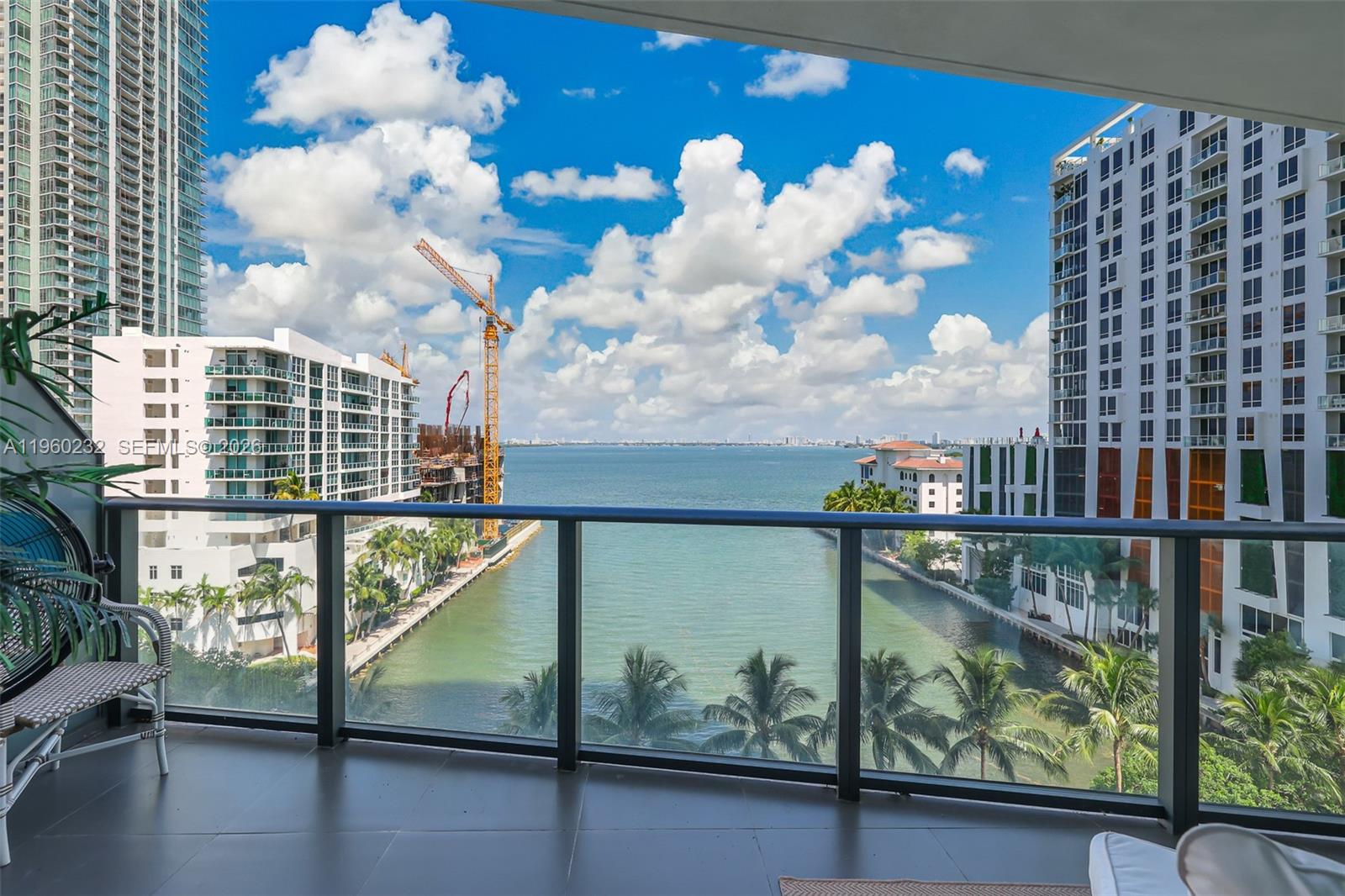 A balcony view overlooking a canal, high-rise buildings, a construction crane, and the ocean — 460 NE 28 # 704, Miami FL 33137, MIAMI, FL