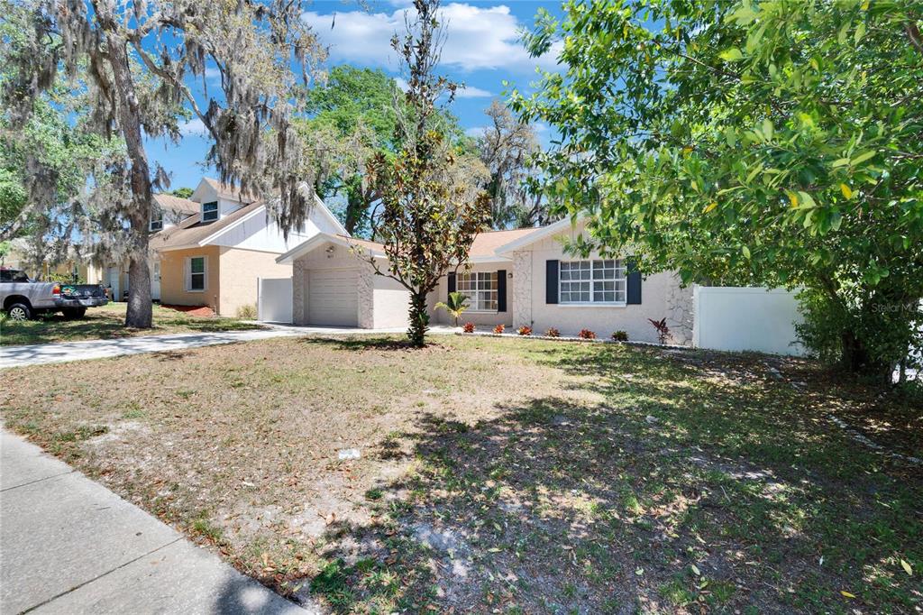 A single-story house with a garage, light-colored siding, and a large tree in the yard — 9613 N 46TH STREET, TAMPA, FL