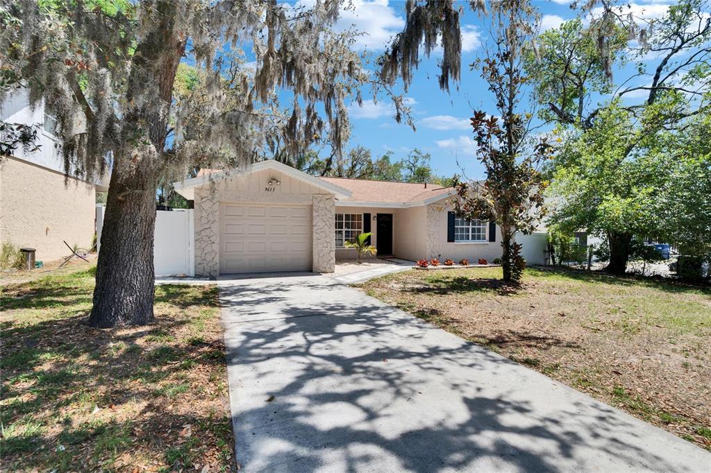 A single-story house with a concrete driveway, stone facade, and large trees with Spanish moss — 9613 N 46TH STREET, TAMPA, FL