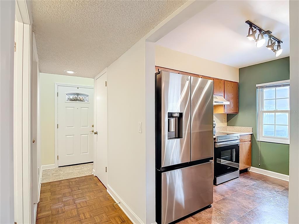 A kitchen with stainless steel appliances and wood cabinets opens into a tiled entryway — 16851 LE CLARE SHORES DRIVE, TAMPA, FL