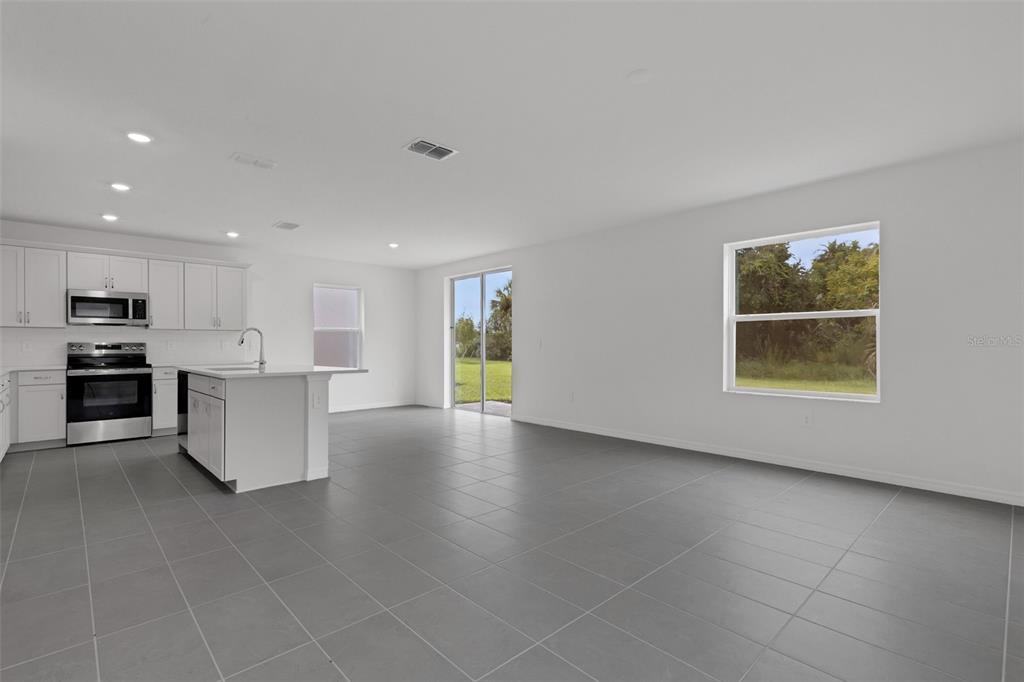 A modern kitchen and living area with white cabinets, a center island, and gray tile flooring — 4328 OUTHAUL RUN, PALMETTO, FL