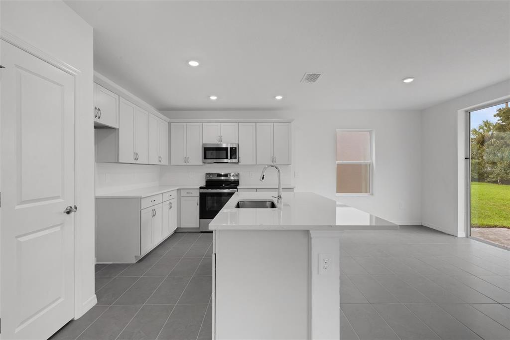 A modern kitchen features white cabinets, quartz countertops, a center island, and gray tile flooring — 4328 OUTHAUL RUN, PALMETTO, FL