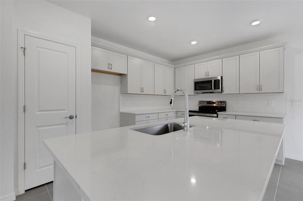 A modern kitchen features white cabinetry, a large quartz island with a sink, and stainless appliances — 4328 OUTHAUL RUN, PALMETTO, FL