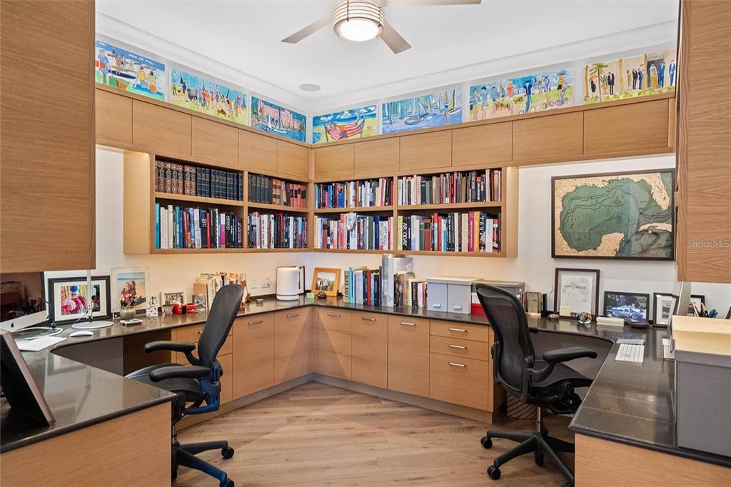 A home office features L-shaped wooden desks, built-in bookshelves, and a series of framed artwork — 400 BEACH DRIVE NE UNIT 401, ST PETERSBURG, FL