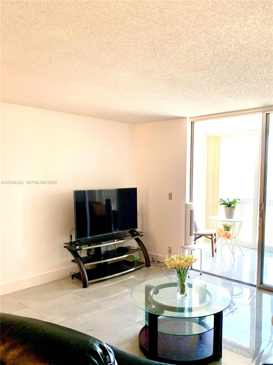 A living room features a glass coffee table, a television on a stand, and a balcony — 501 NE 14th Ave # 601, Hallandale Beach FL 33009, HALLANDALE BEACH, FL