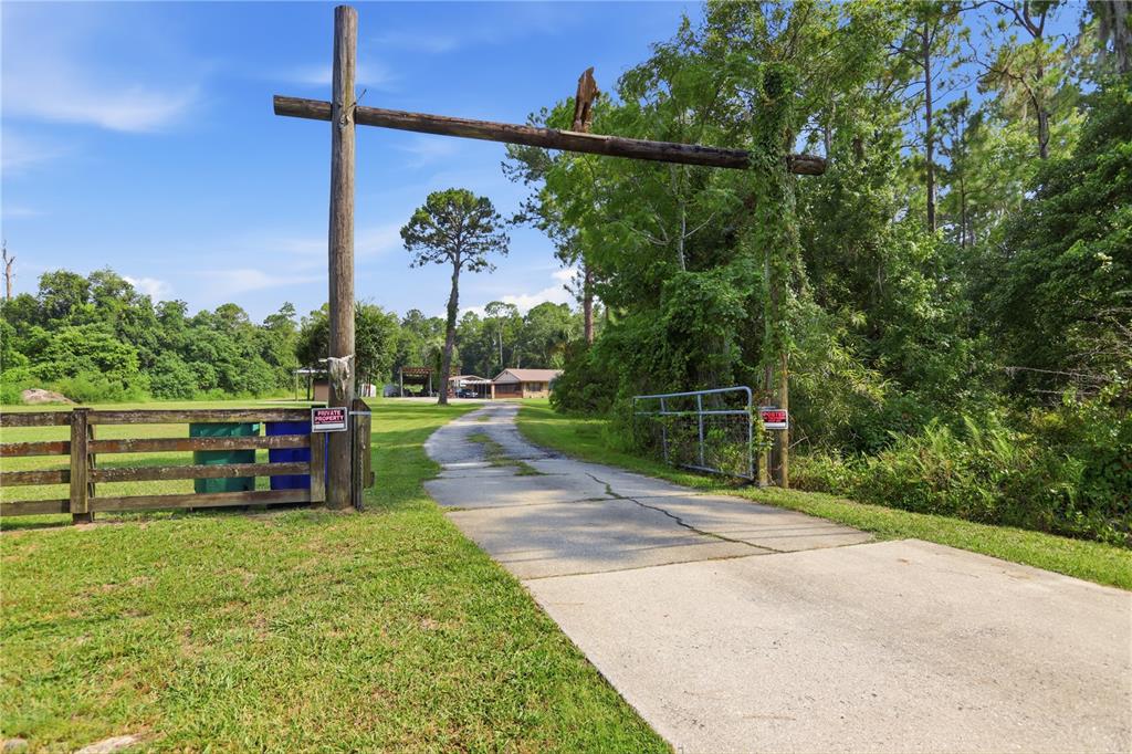 A concrete driveway leads through a wooden gate toward a house on a rural property — 1820 OLD DAYTONA ROAD, DELAND, FL