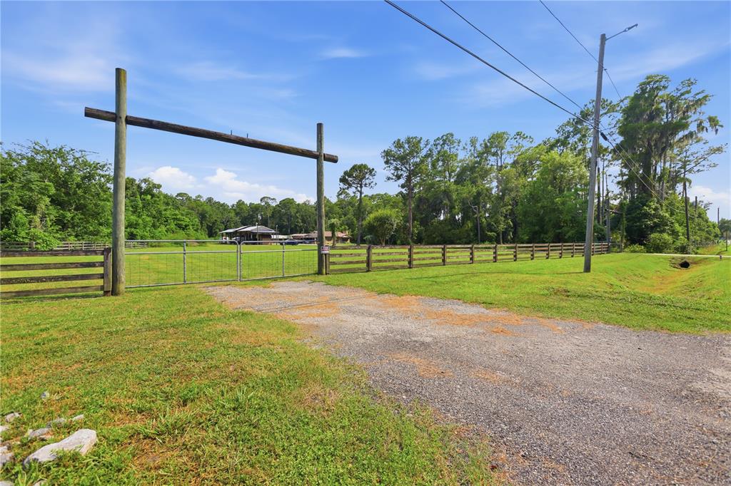 A gravel driveway leads to a gated entrance with a wooden archway on a grassy lot — 1820 OLD DAYTONA ROAD, DELAND, FL