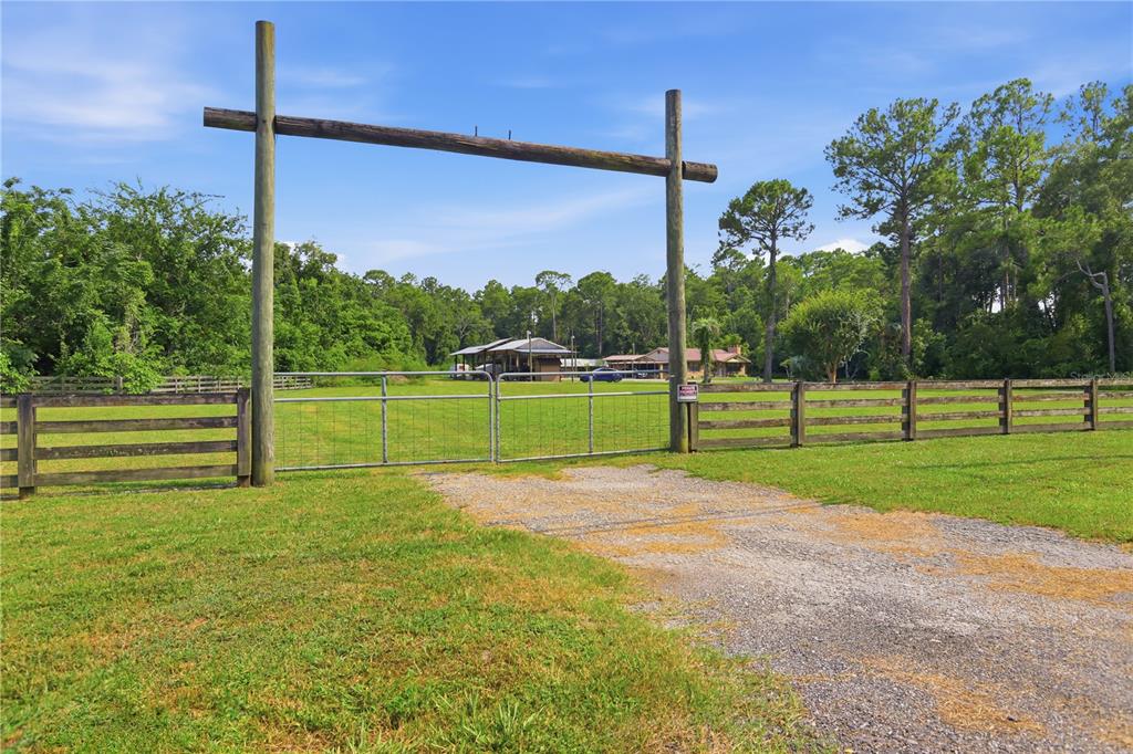 A gravel driveway leads to a metal gate framed by two tall wooden posts — 1820 OLD DAYTONA ROAD, DELAND, FL