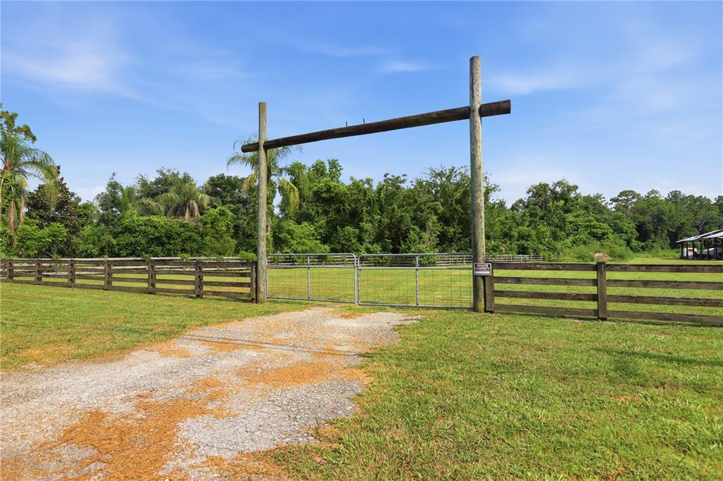 A gravel driveway leads to a metal gate framed by two tall wooden posts — 1820 OLD DAYTONA ROAD, DELAND, FL