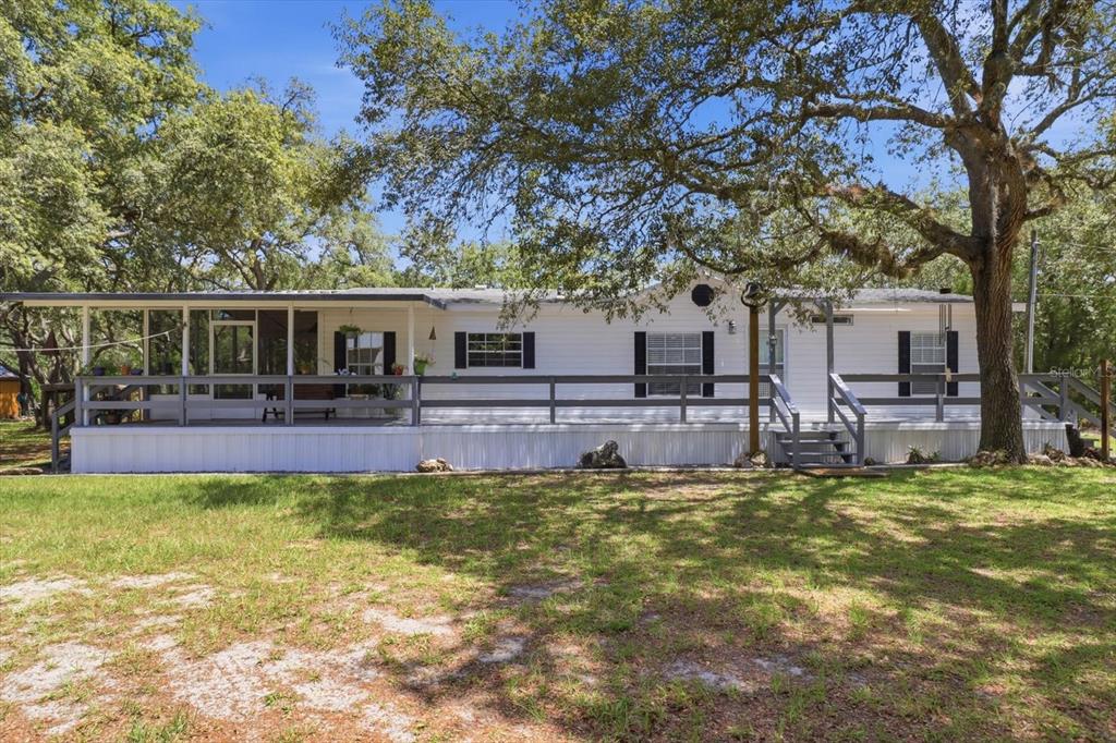 A white mobile home with a wooden deck sits on a grassy lot with trees — 7298 S RAMA AVENUE, LECANTO, FL