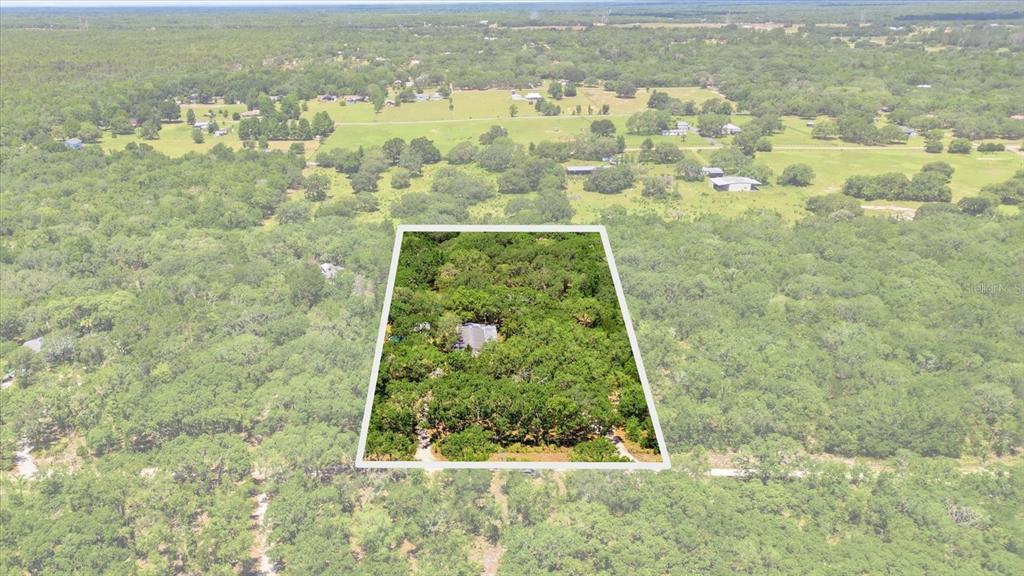 An aerial view shows a house nestled within a wooded lot outlined in white — 7298 S RAMA AVENUE, LECANTO, FL