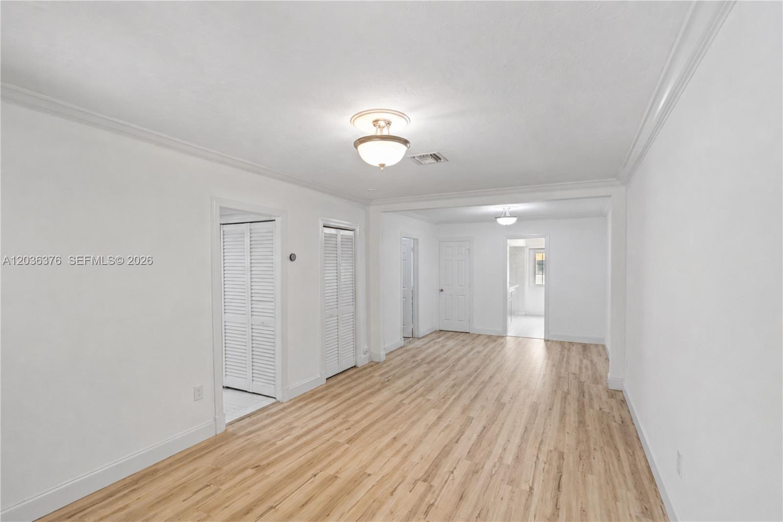 An empty room features white walls, light wood-look flooring, and multiple doorways with louvered doors — 2530 SW 27th St # 2532, Miami FL 33133, MIAMI, FL