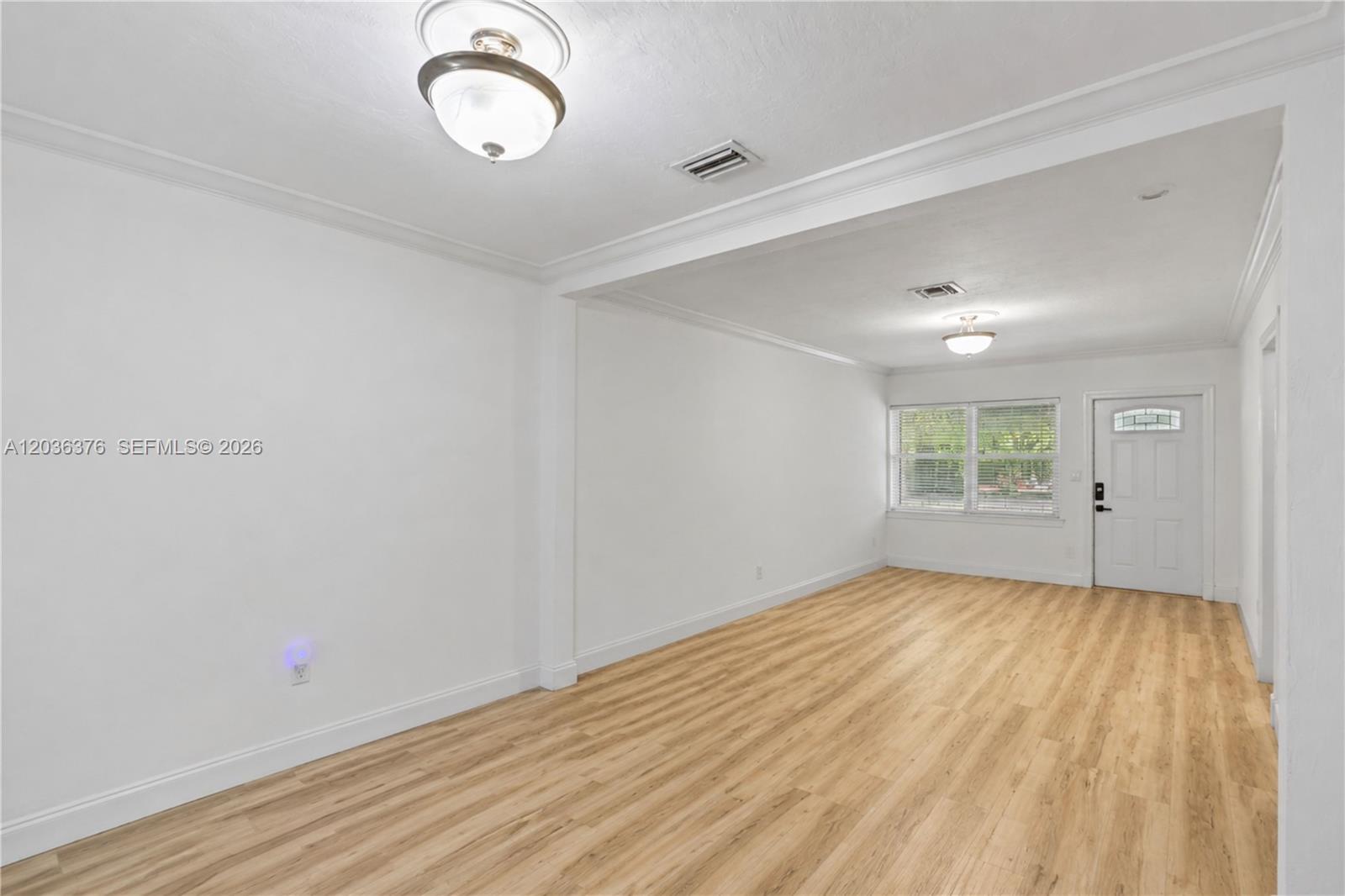 An empty room features white walls, crown molding, light wood-look flooring, and two ceiling lights — 2530 SW 27th St # 2532, Miami FL 33133, MIAMI, FL