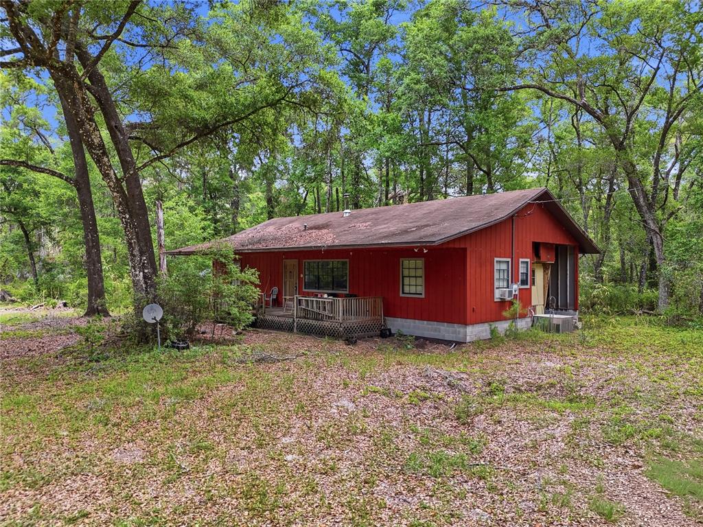 A red wooden house with a deck sits in a wooded area — 8009 SW 131ST TERRACE, ARCHER, FL