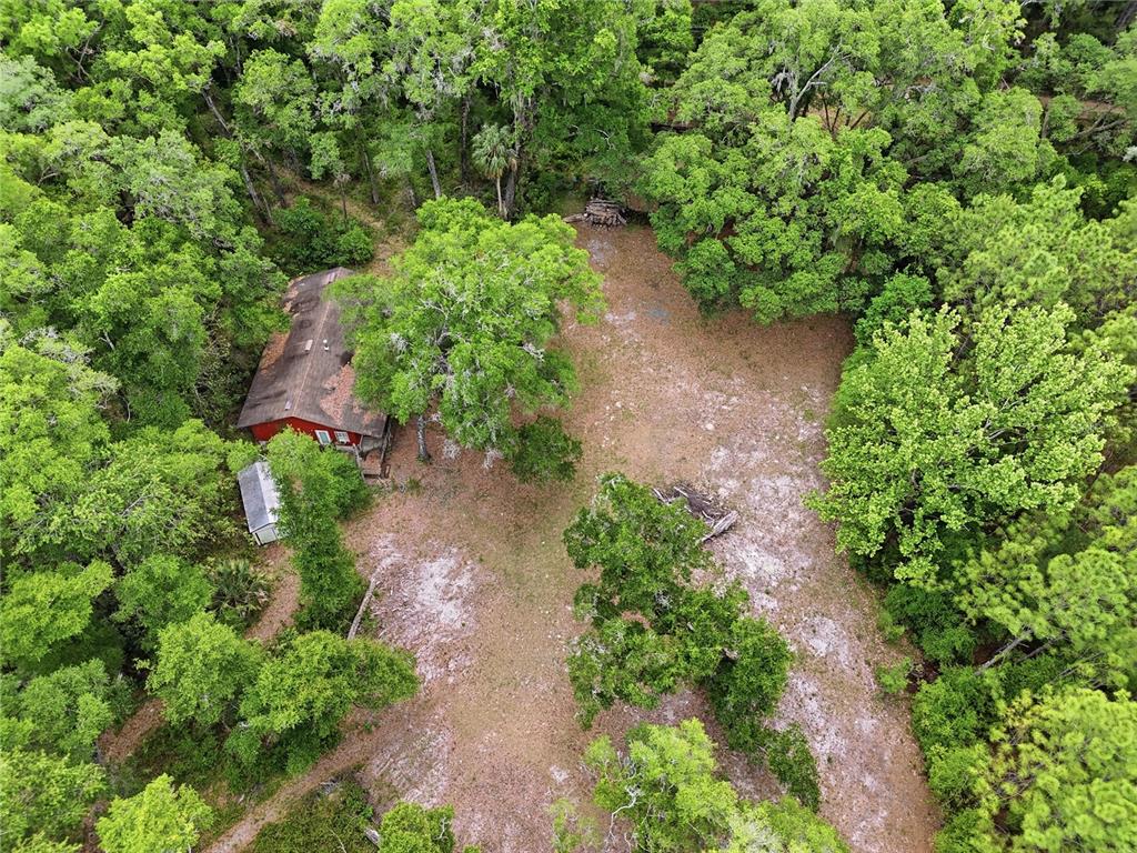 A red house with a wooden deck sits on a grassy lot near trees — 8009 SW 131ST TERRACE, ARCHER, FL
